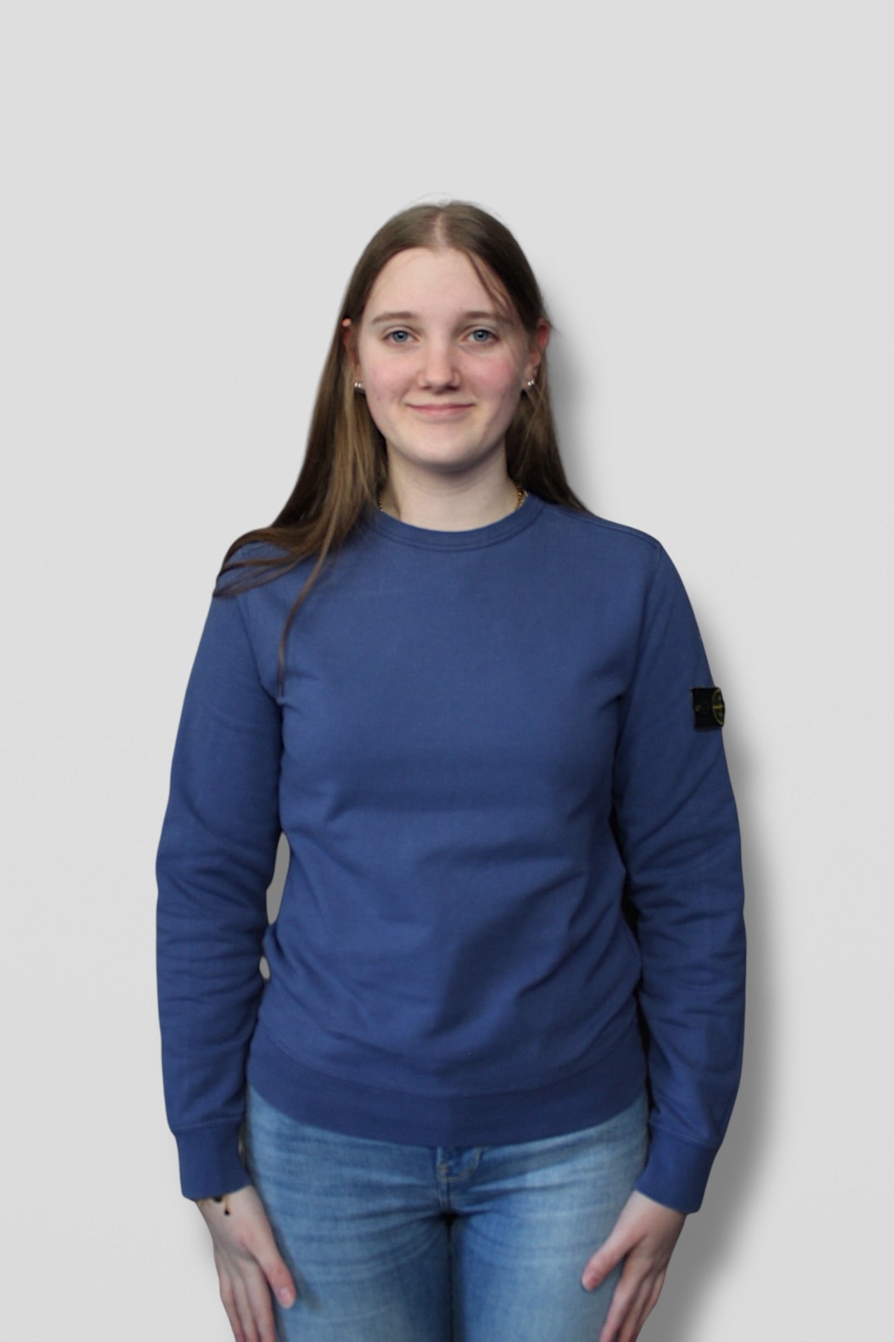 Person wearing a blue sweatshirt with a brand logo on a plain background