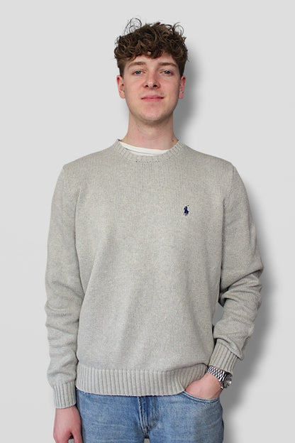 Man wearing a gray sweater with a small logo, standing against a plain background