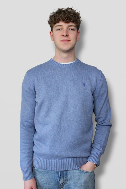 Man wearing a blue sweater with a logo on a plain background