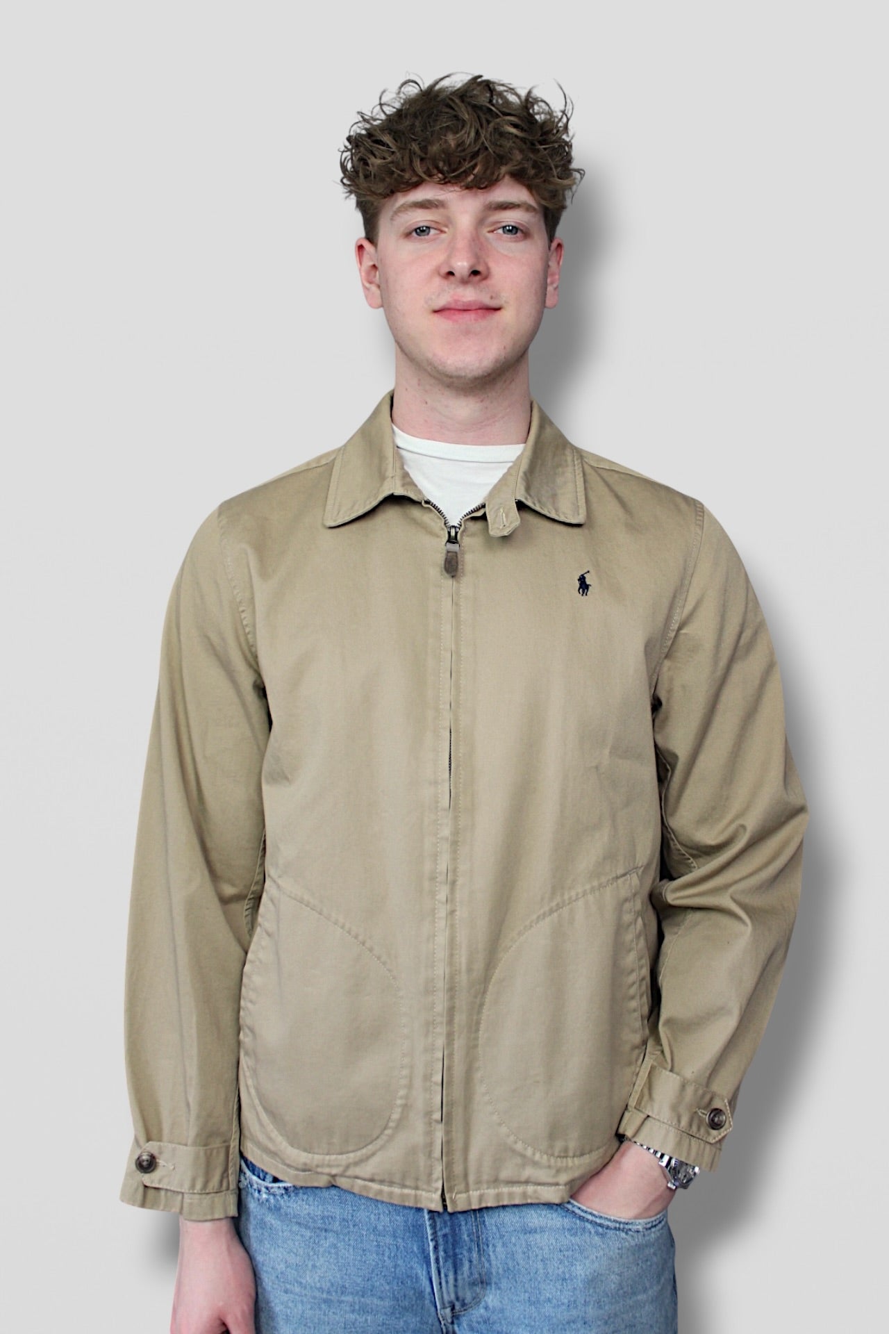 Man wearing a beige jacket with a logo on a plain background