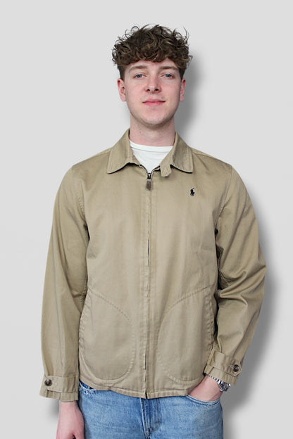 Man wearing a beige jacket with a logo on a plain background