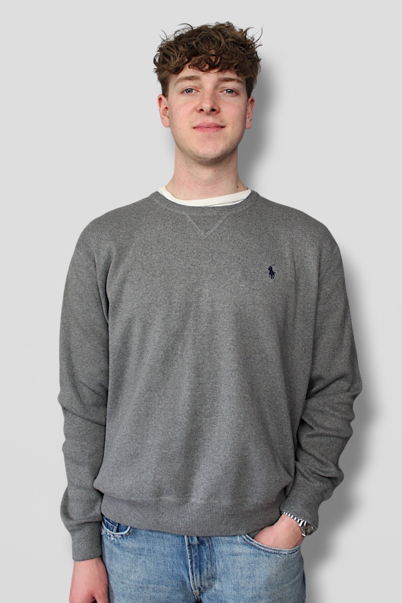 Person wearing a gray sweatshirt with a logo on a plain background
