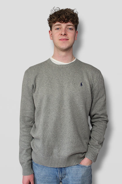Man wearing a gray sweater with a small logo on a plain background