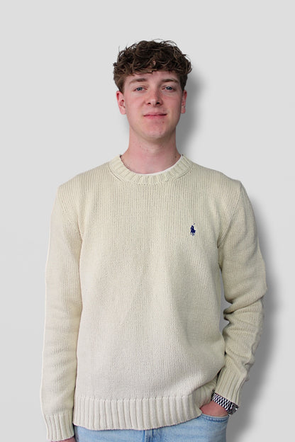 Person wearing a cream sweater with a logo on a plain background