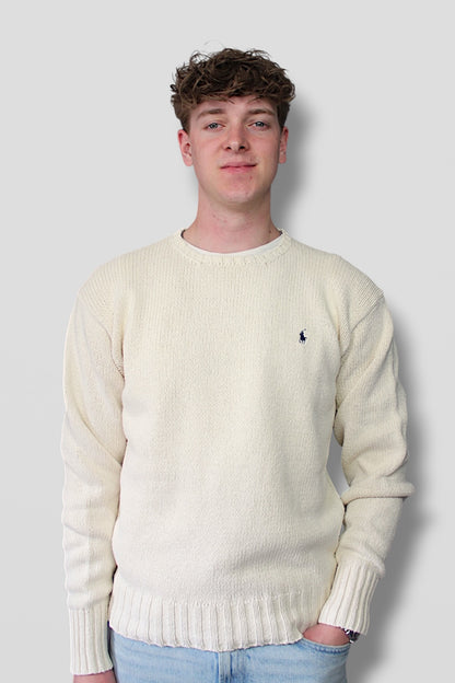 Man wearing a cream sweater with a small logo on a plain background