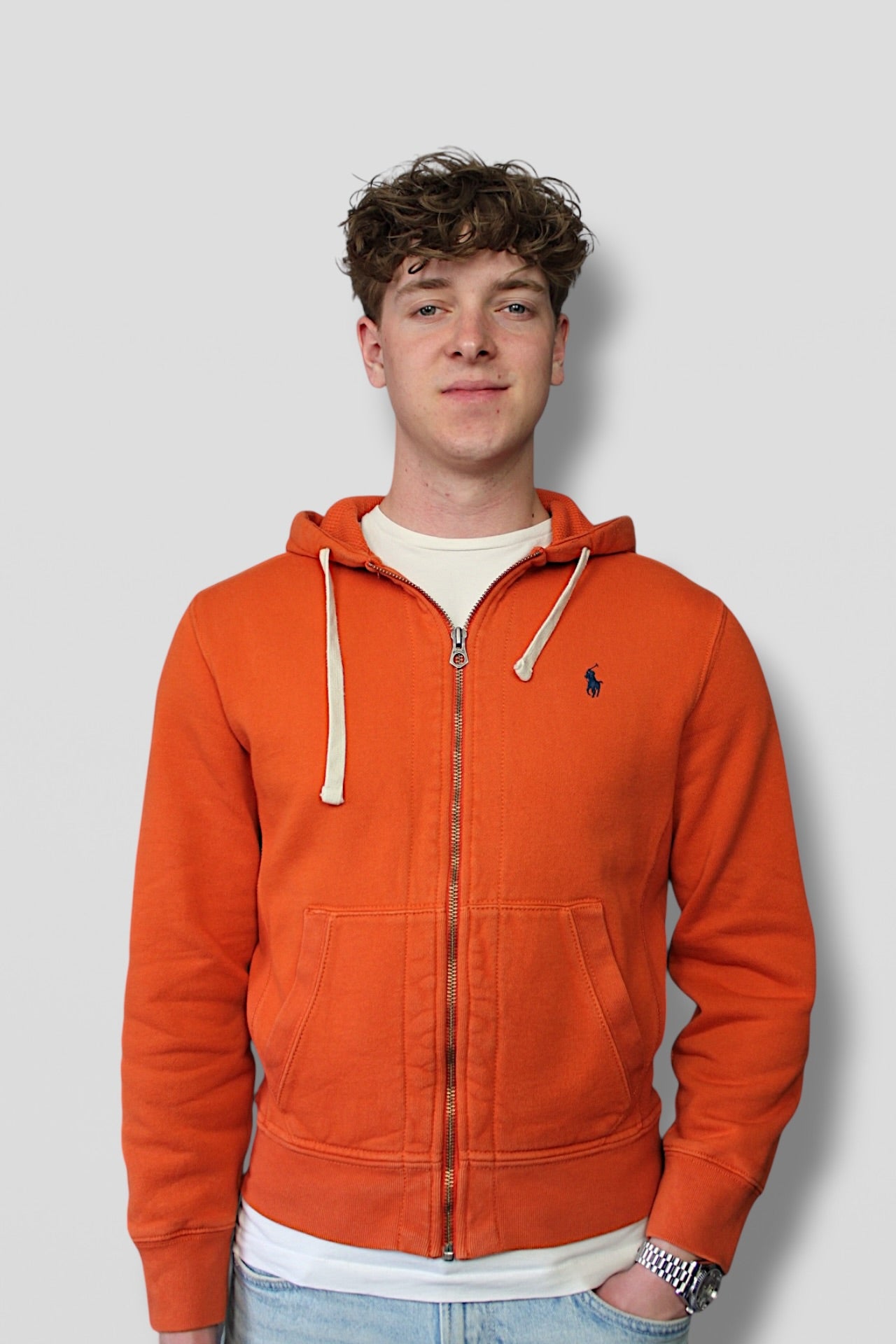 Person wearing an orange hoodie with a visible brand logo on a plain background