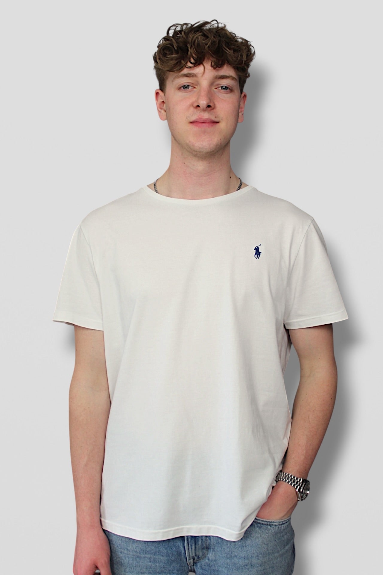 Person wearing a white t-shirt with a small logo on a plain background