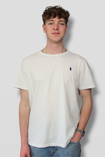 Person wearing a white t-shirt with a small logo on a plain background