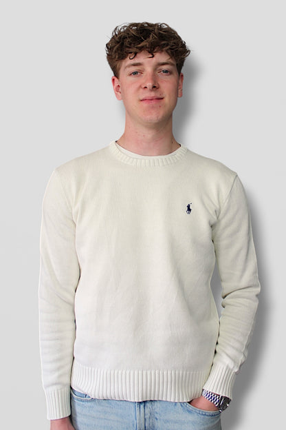 Man wearing a white sweater with a logo against a plain background