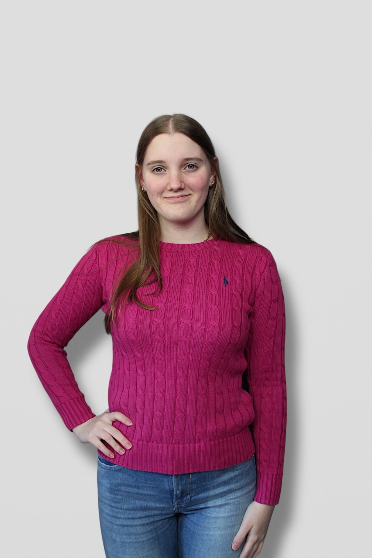 Person wearing a pink sweater with a logo on a plain background
